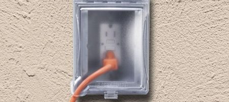 Outdoor GFCI electrical outlet with weatherproof cover safely powering equipment in backyard